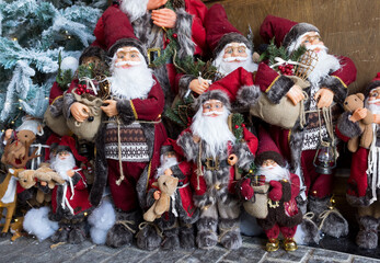 Stack of Santa Claus toys near decorated frosted Christmas Tree.