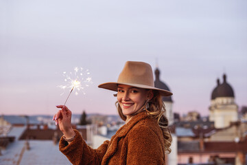 Happy smiling woman holding sparkler, posing in European city. Christmas, New Year, winter holidays conception. Outdoor portrait. Copy, empty space for text