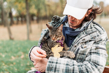 Owner holding cute, striped cat inside his jacket, outdoors photo