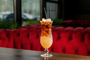 A layered alcoholic cocktail in a hurricane glass, with ice and straw, at the bar