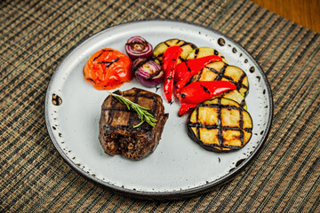 Filet mignon with grilled vegetables and rosemary garnish on a white plate