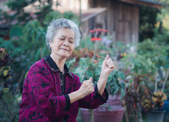 A senior woman with short white hair, smiling, looking away, and exercises while standing in a garden. Space for text. Concept of aged people and healthcare