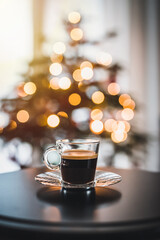 Glass cup of coffee close up. In the background a Christmas tree and Christmas lights.