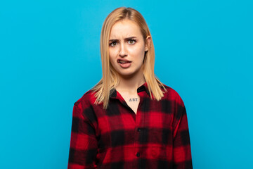 young blonde woman feeling puzzled and confused, with a dumb, stunned expression looking at...
