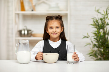 smiling cute little girl in school uniform having breakfast: cereal with the milk in the kitchen. healthy breakfast