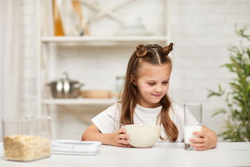 adorable little girl eating breakfast: cereal with the milk in the kitchen. healthy breakfast