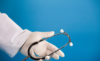 Stethoscope in doctor's hand with surgical glove and blue background.