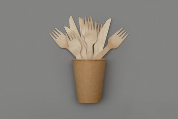 Wooden fork and knife in paper cup on gray background, top view. Eco friendly disposable tableware from natural material. Ecological concept.