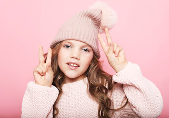 cute little girl in pink sweater and winter hat showing victory sign