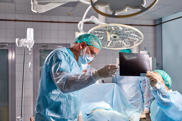 friendly team of confident concentrated caucasian surgeons in operating room with surgery equipment,modern medical background. healthcare, medicine concept