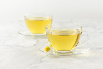 glass cups with chamomile tea on a light marble background.
