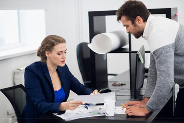 A senior manager explaining something to her team member, while sitting at her desk in the office.