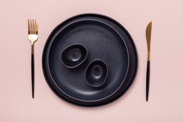Set of black ceramic plates and cutlery on pastel pink background. Copy space for your text