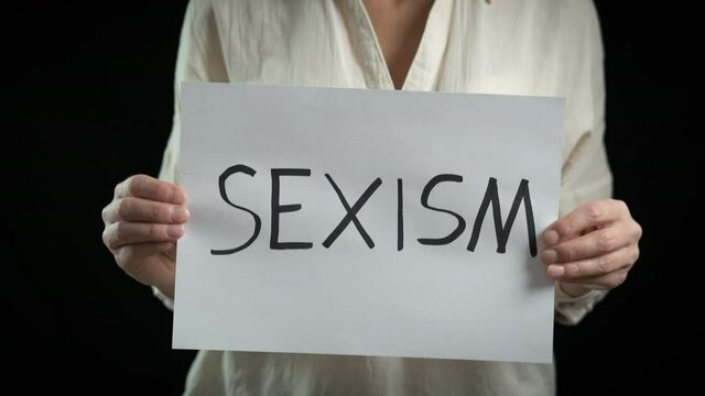 Sexism resistation. A woman with a poster support anti sexism movement on the black background.