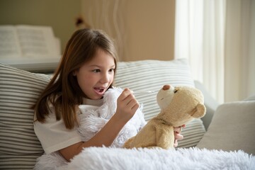 Cute, sick girl is playing doctor, measuring a teddy bear's fever.