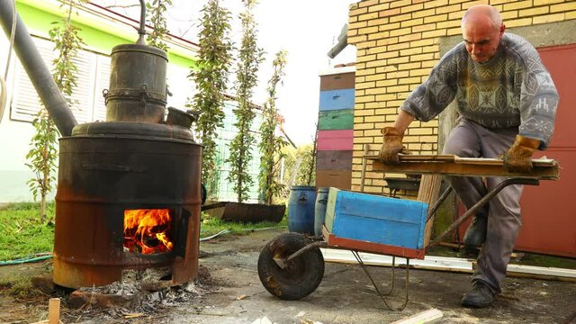 Farmer is cutting old wooden window using saw, bucksaw for fire under homemade distillery to making moonshine schnapps, alcoholic beverages.