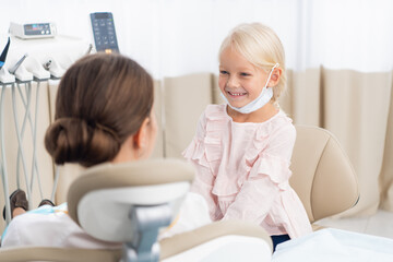 Obraz premium Adorable little girl sitting and making an examination of a female doctor, the doctor is sitting in a dentist chair. Dentist and child in a dentist office. Little girl in the dentists office.