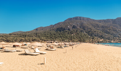Popular resort Iztuzu beach with luxury sun umbrellas and loungers and fine yellow sand awaits vacationers and tourists in Turkey, near Dalyan. Sea paradise and relaxation concept