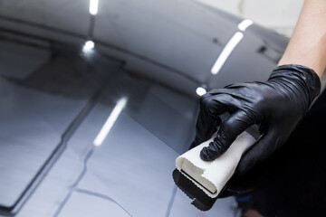 The process of applying a nano-ceramic coating on the car's hood by a male worker with a sponge and...