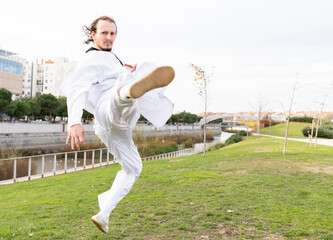 man practices judo in the park, with judo clothes on a cloudy day, jumps and makes plenty,