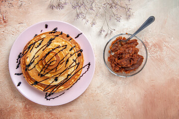 Above view of stuffy pancakes decorated with chocolate syrup and apple jam on a white background