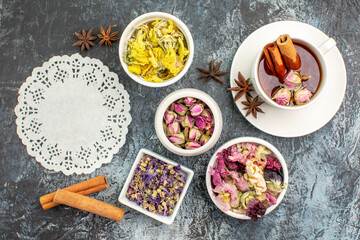 top view of a piece of lace and herbal tea with dry flowers and cinnamon sticks on grey background
