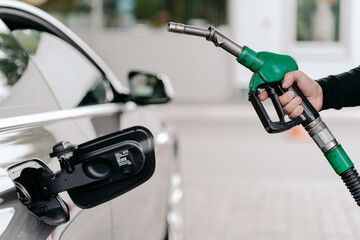 Cropped shot of mans hand pumping gasoline fuel in car at gas station. Auto being filled with...