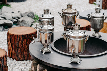 Antique copper samovars on round surface with wooden stumps outdoor. Tea drinking party concept. Russian tradition