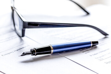 Pen and glasses lying on signed documents on office desk