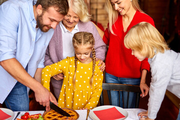 family carving christmas pie together, preparing and decorating table, on the eve of new year, child girl is surrounded by parents and grandparents