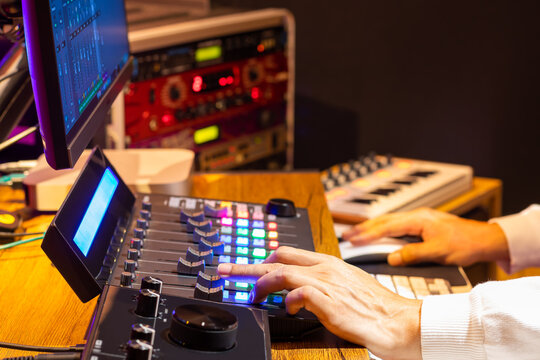 professional producer hands adjusting control surface fader for mixing audio and video on computer in post production and broadcasting studio