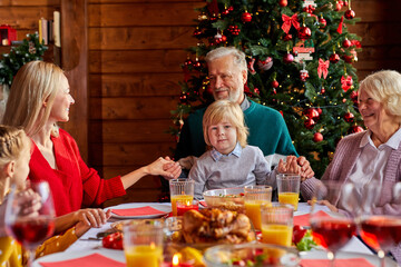 family having christmas dinner and praying before meal, multi-generation family enjoy celebrating...