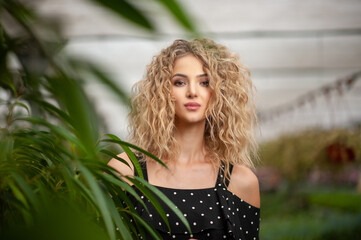 Naklejka premium portrait of a beautiful young girl standing among green plants looking at the camera and smiling