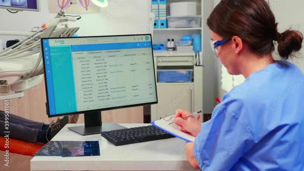 Aufkleber orthodontist nurse looking at list with appointments in computer and taking notes on clipboard while