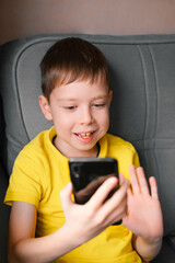 boy with a mobile phone speaks by video calling at home.  the schoolboy  communicates via video link. Video chatting at home. Modern technology and children