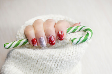 A female hand with a red New Year's manicure holds a candy cane.
