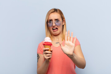 young blonde woman feeling terrified, backing off and screaming in horror and panic, reacting to a...