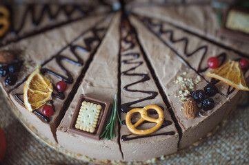 chocolate cake decorated with chocolate, cookies and dried orange. A round mousse cake, cut into pieces, is on a brown kraft tablecloth.