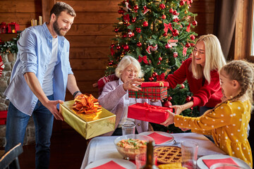 senior woman gets christmas gifts from her children and grandchildren, shine with happiness, she is glad to celebrate new year with loved ones