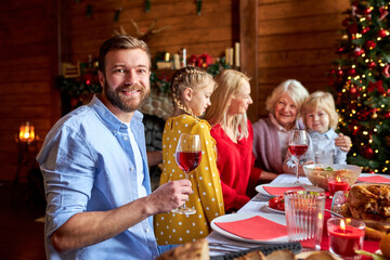 guy holding wine glass in hands with family in the background, celebrating christmas