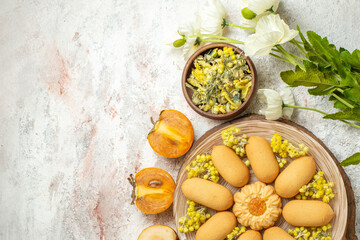 overhead shot of cookie and white flowers and a bowl of herbs and fruits on marble background