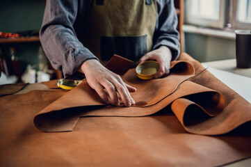 The initial stage of production of leather shoes, a young guy lays out the leather on the table for...