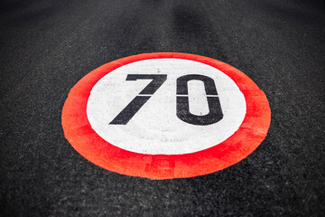 70km per hour speed limit sign painted on dark asphalting road.