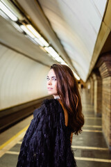 elegant woman standing on metro platform and looking at camera