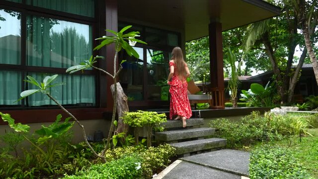 Happy Travel Woman In Dress Going To Wooden Luxury Villas In Modern Tropical Resort Among Jungle With Green Trees And Palm. Tourist Rented Home For Vacation, Relax And Enjoy Summer Holiday In Thailand