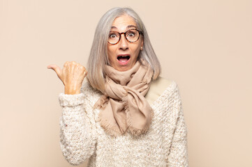 middle age woman looking astonished in disbelief, pointing at object on the side and saying wow,...