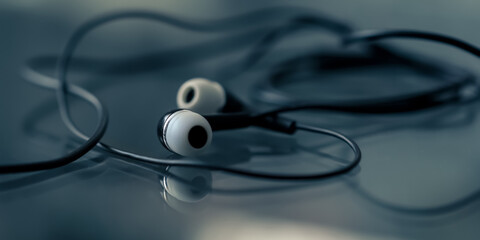 Headphones with black cord and white earbuds lying on table with glass surface