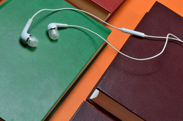 white vacuum headphones lie on books laid out on an orange background. audiobook concept.