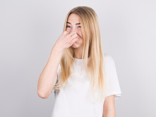 Young woman with disgust on his face pinches nose on white background. Negative emotion facial expression.