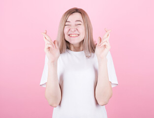 Pleased cheerful blonde woman puts all efforts in wishing good luck, crosses fingers, isolated over pink background.